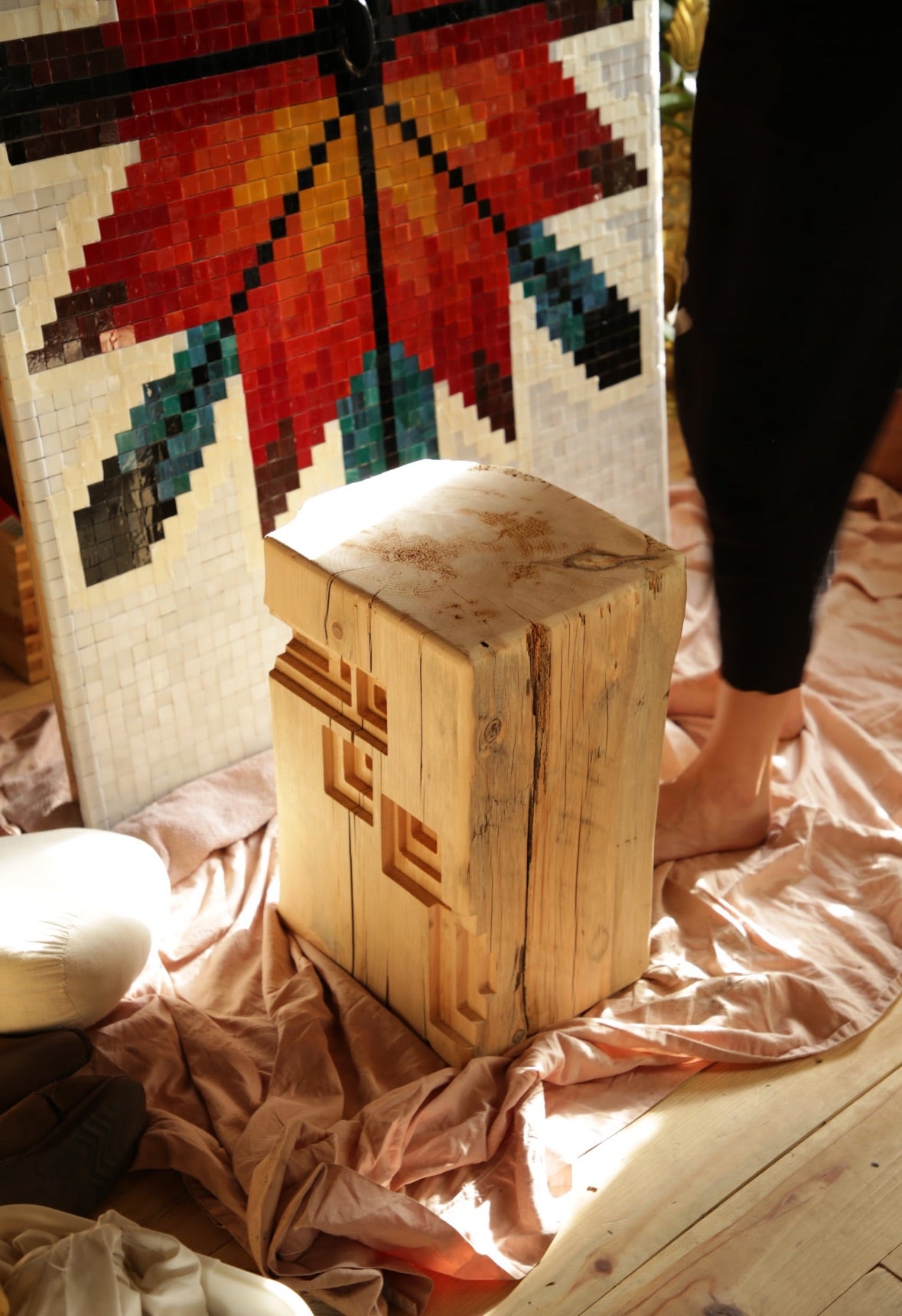 Wooden stool with geometric design in front of a colorful tapestry